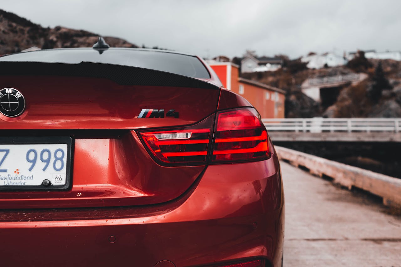 Rear view of a BMW M4 in a coastal setting, highlighting its modern design and vibrant color.